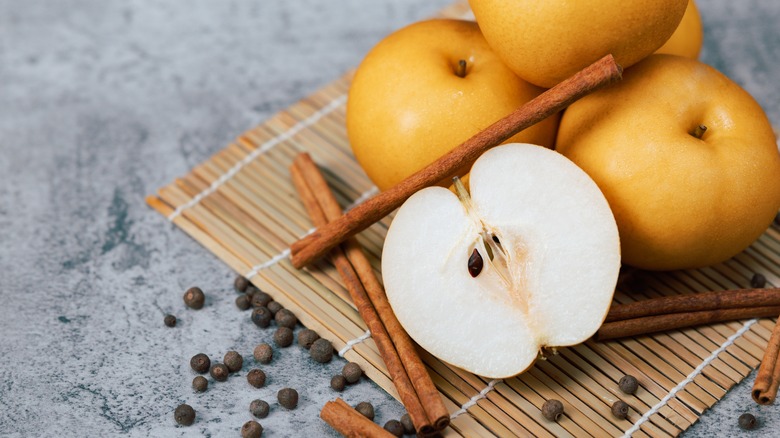 pears, allspice, and cinnamon sticks on bamboo mat on gray background