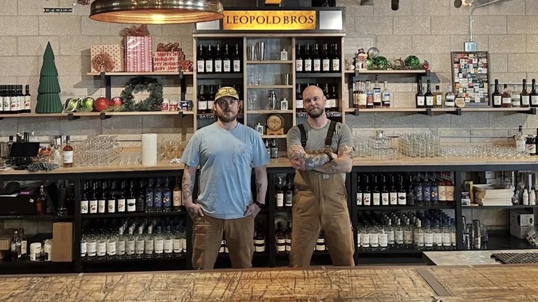 Two men standing behind a bar counter with a Leopold Bros sign
