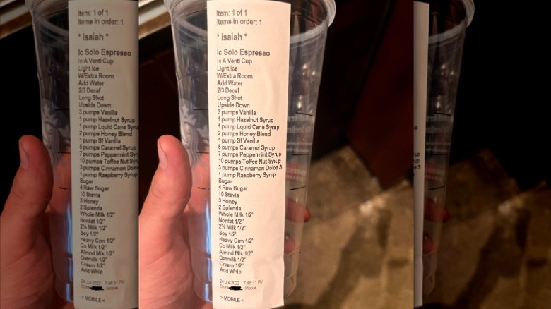 A hand holding up an empty Starbucks cup, with an order sticker on it that has dozens of lines of modifications