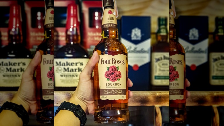 A person's hand holding a bottle of Four Roses Yellow Label whiskey
