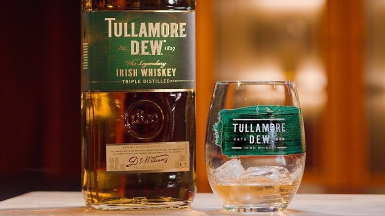 A glass of Tullamore D.E.W. whiskey in a glass with ice next to bottle