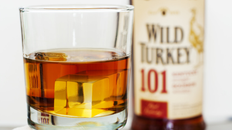 A glass of Wild Turkey 101 whiskey in a glass with ice in front of the bottle