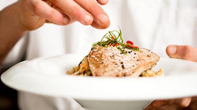 Chef's hand adding final touch to tuna appetizer in white bowl