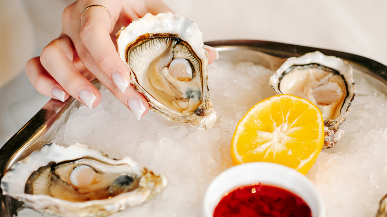 hand holding oyster over dish with ice, lemon, and dip