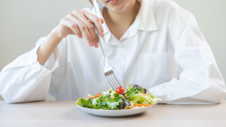 unhappy woman sat at table eating salad