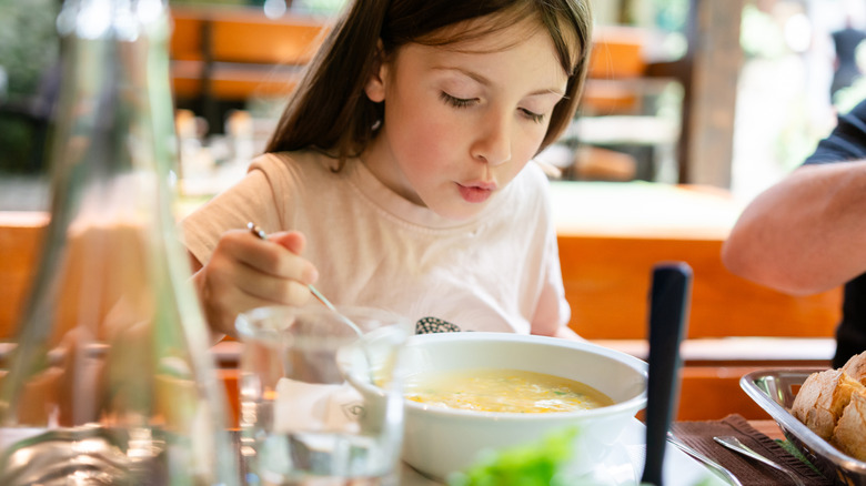 Little girl eating hot soup while sitting at the restaurant