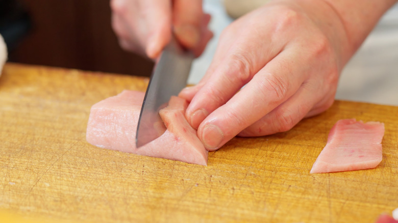 close up of hands cutting swordfish meat on wooden surface