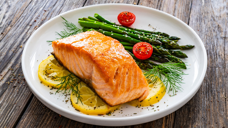 Salmon fillet with asparagus, tomatoes, dill and lemon on plate
