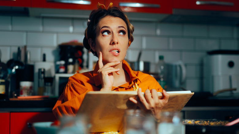 Woman sitting in a kitchen reading cookbook with inquisitive look