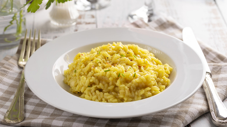 Risotto alla milanese in a white plate with fork and knife on the side