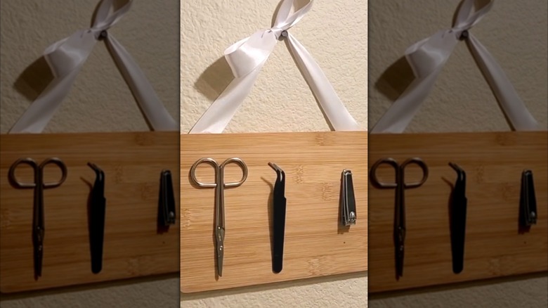 Wooden magnetic board holding scissors, tweezers, and nail clipper hung on wall with white ribbon