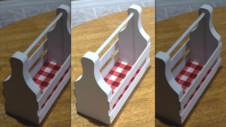 A white kitchen caddy with red checkered lining on the bottom sitting on wood table