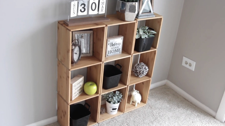 Wooden cube style organizer holding potted plants, clock, and decorations in white room