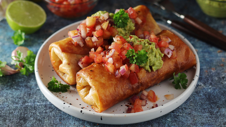 Chiminchangas on plate covered in pico de gaillo and guacamole