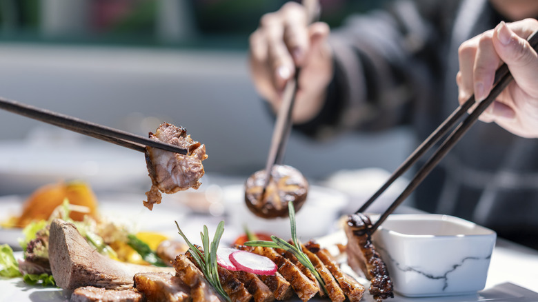 three people using chopsticks to pick up meat