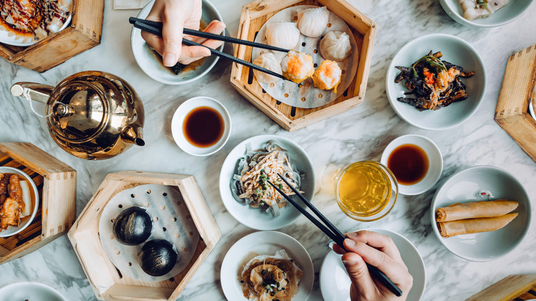 multiple plates of chinese food with two hands holding chopsticks