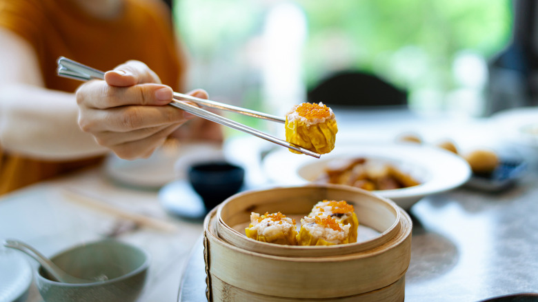 a person picking up a dumpling from a wood basket