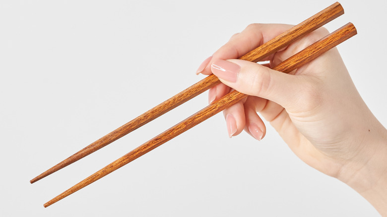 a hand holding chopsticks on a white background