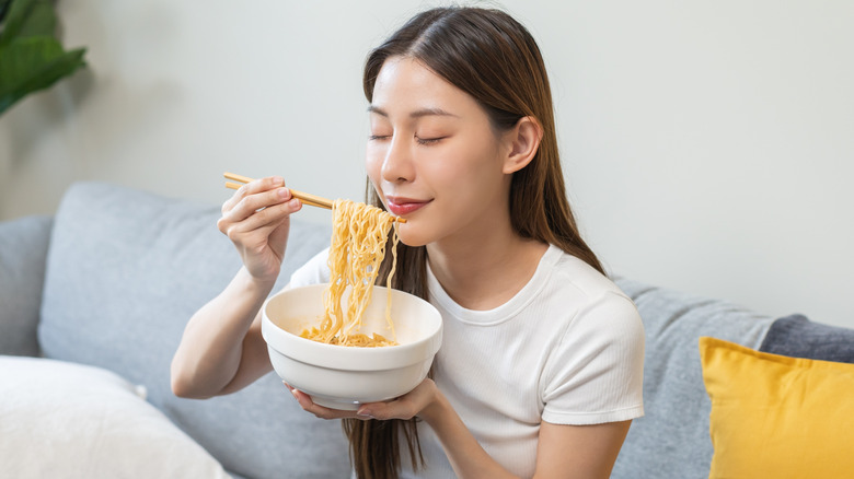 a woman holding and eating a bowl of ramen