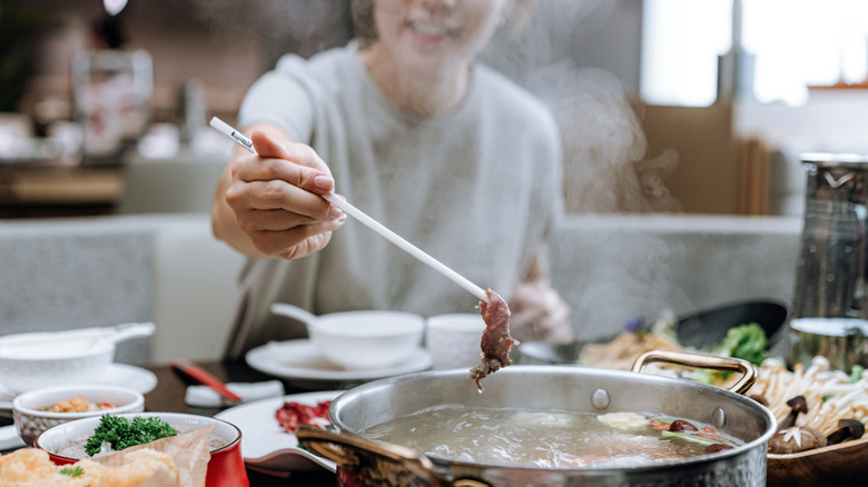 a person placing meat in a hot pot
