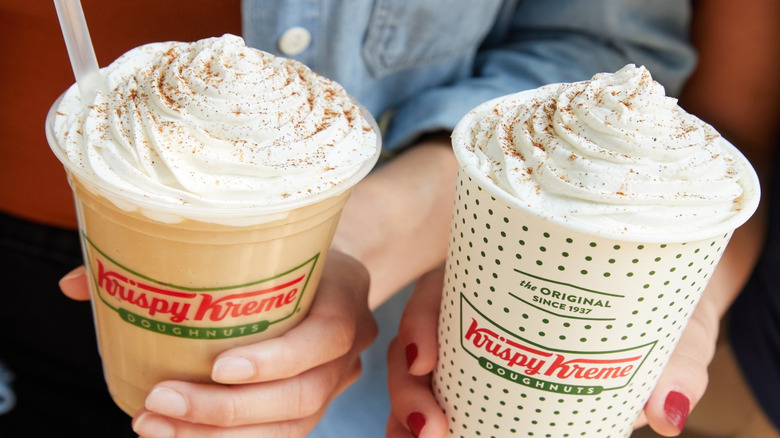 Hands holding Krispy Kreme Frozen Pumpkin Spice Latte and hot Pumpkin Spice Latte in paper cups