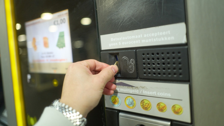 Hand putting coins in a vending machine