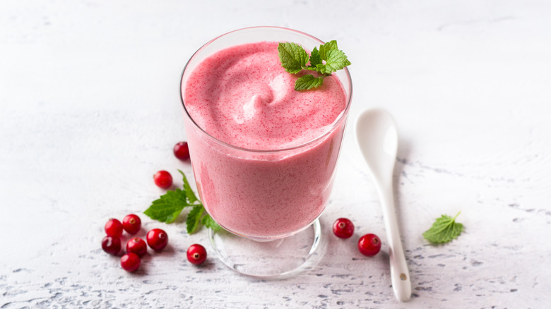 cranberry mousse in glass with garnish next to white spoon and cranberries