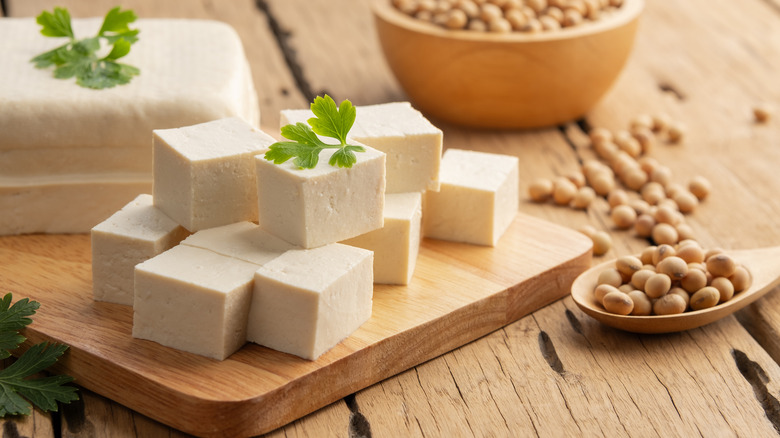 slicked block of tofu on cutting board with bowl of soybeans