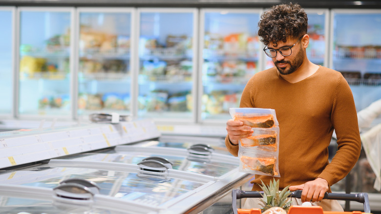 Customer choosing pre-packaged frozen fish in a supermarket aisle