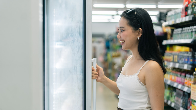 woman opening freezer door in supermarket aisle