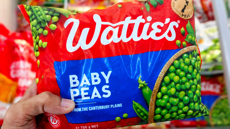 A hand holds a bag of frozen baby peas over freezer section