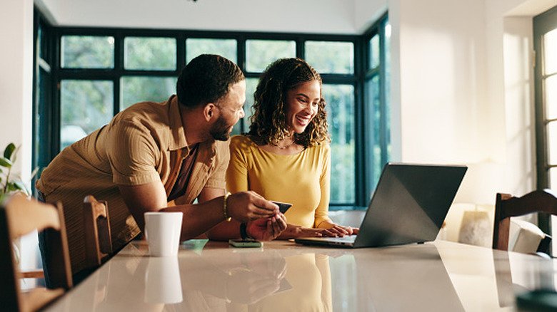 young African-American couple, at a gleaming counter or kitchen island, making an online purchase on their laptop