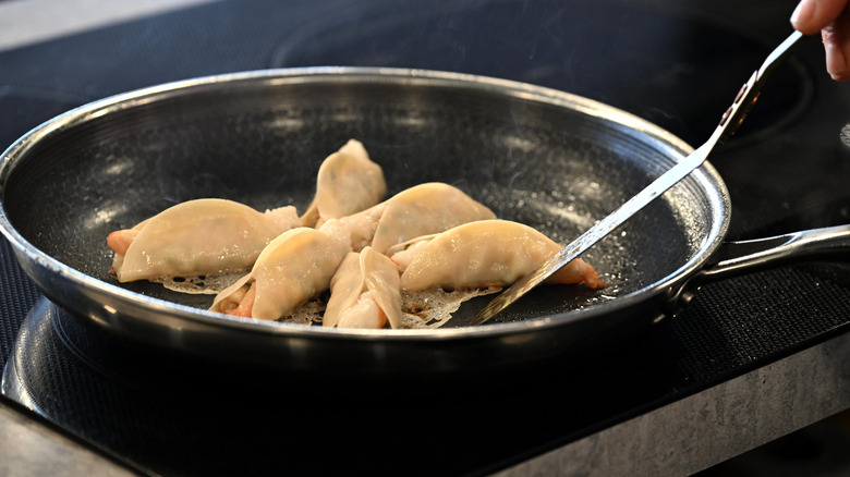 Dumplings frying in a HexClad pan, with a hand tending them with a metal spatula