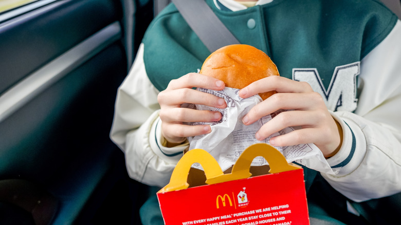 person in green and white varsity jacket holds a McDonald's hamburger, close up