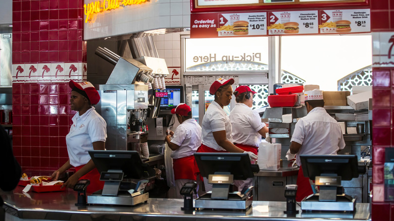 Inside an In-N-Out Burger restaurant, employees in uniform work at the counter and in the kitchen