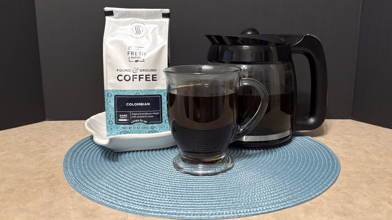 The Fresh Market Colombian coffee in bag, pot, and glass on teal placemat and black background