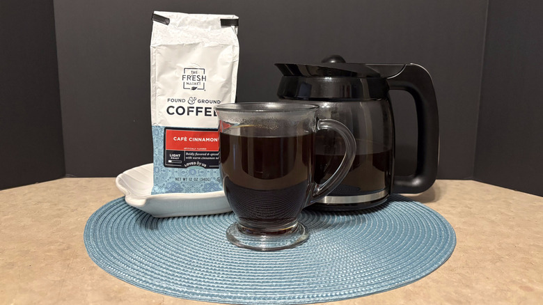 The Fresh Market café cinnamon coffee in bag, pot, and glass on teal placemat and black background