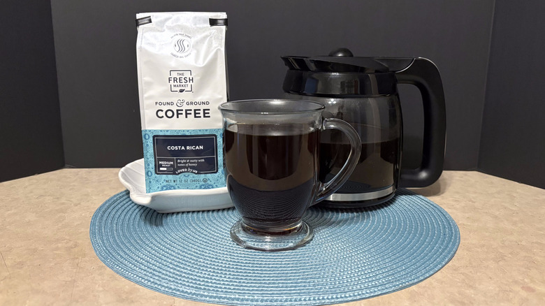 The Fresh Market Costa Rican coffee in bag, pot, and glass on teal placemat and black background