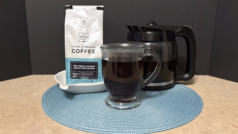 The Fresh Market signature blend coffee in bag, pot, and glass on teal placemat and black background