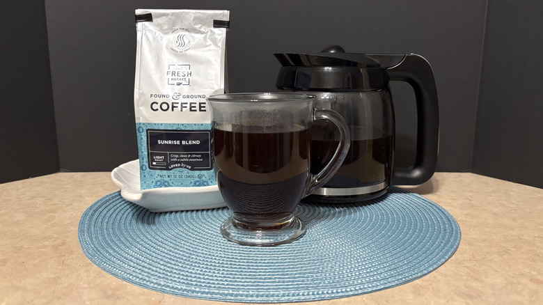 The Fresh Market sunrise blend coffee in bag, pot, and glass on teal placemat and black background