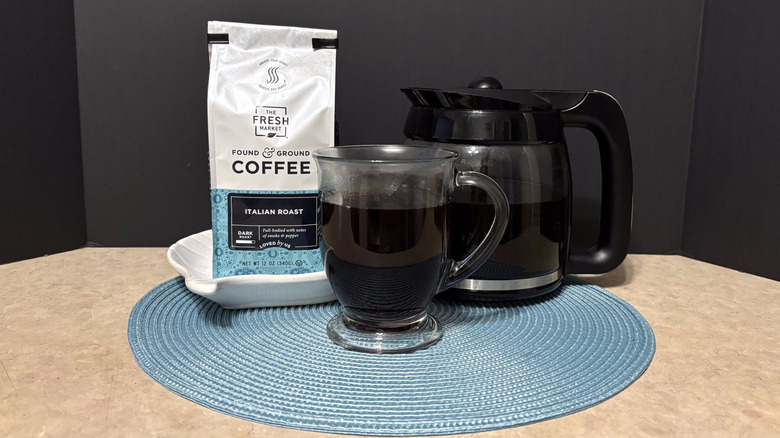 The Fresh Market Italian roast coffee in bag, pot, and glass on teal placemat and black background