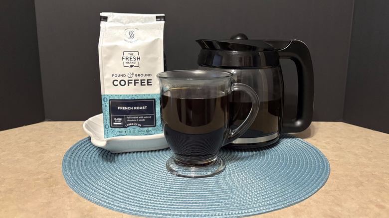 The Fresh Market French roast coffee in bag, pot, and glass on teal placemat and black background