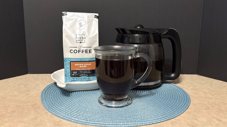 The Fresh Market brown sugar blend coffee in bag, pot, and glass on teal placemat and black background