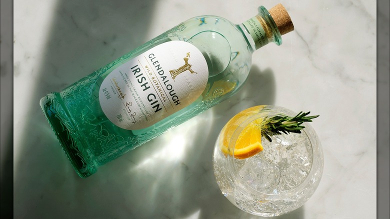 Glendalough Wild Botanical gin bottle and glass with lemon and rosemary garnish on a marble counter
