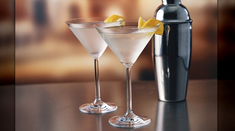 Two martini glasses garnished with a lemon twist with shaker and a twist
