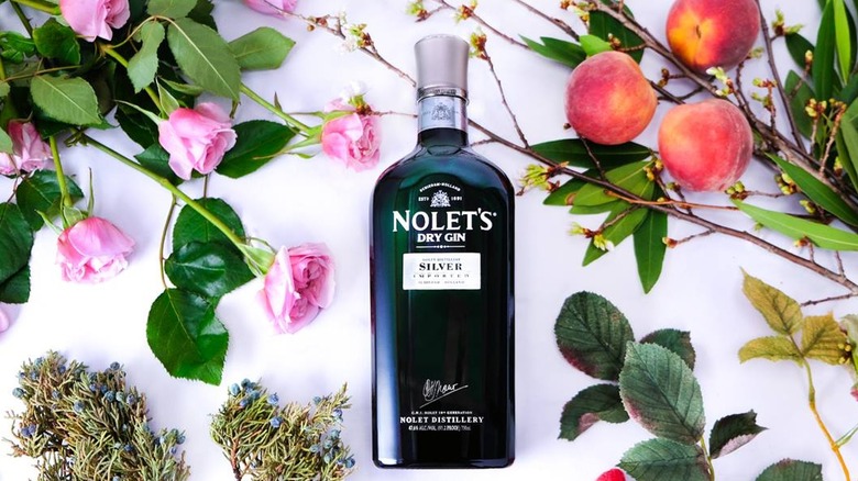 Nolet's Silver gin bottle surrounded by various botanicals including fruit, flowers, and herbs