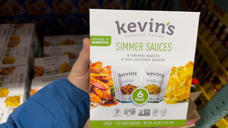 Hand holding Kevin's Natural Foods Simmer Sauces box in front of shelf
