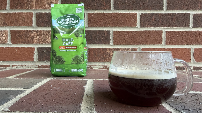 Bag of half-caff ground coffee with pastures illustrated on packaging, set against brick wall