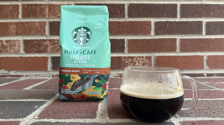 Bag of half-caff ground coffee with image of metallic scoop filled with beans, set against brick wall