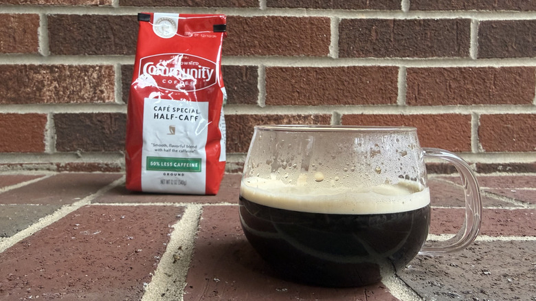 Glossy red bag of half-caff ground coffee, standing in front of brick wall